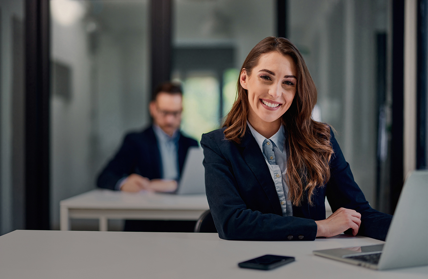 Eine Beraterin sitzt an einem Schreibtisch und wartet lächelnd auf Kund:innen.