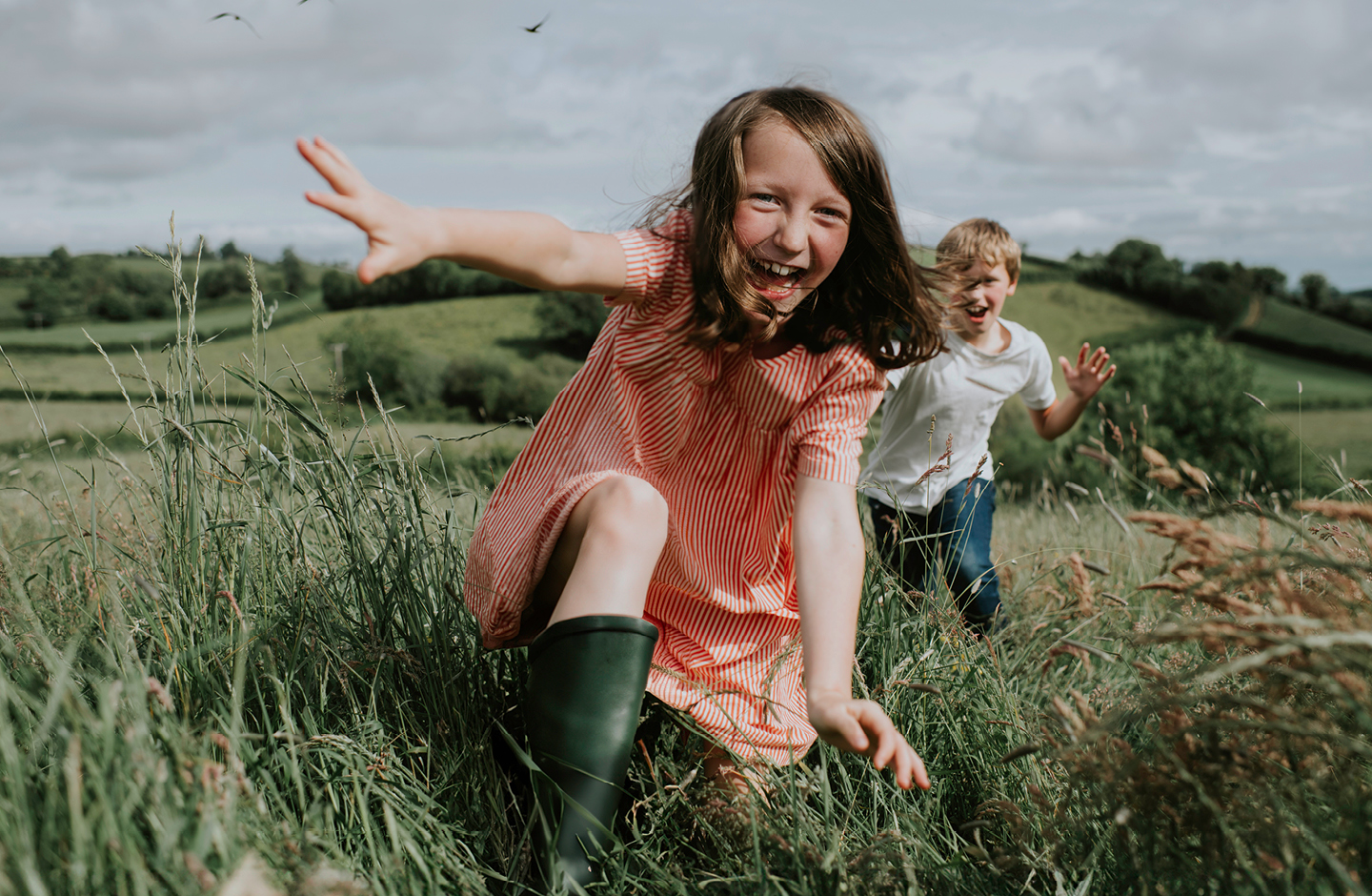 Ein Mädchen und ein Bub laufen über ein Feld auf die Kamera zu. Sie sind ausgelassen und lachen.