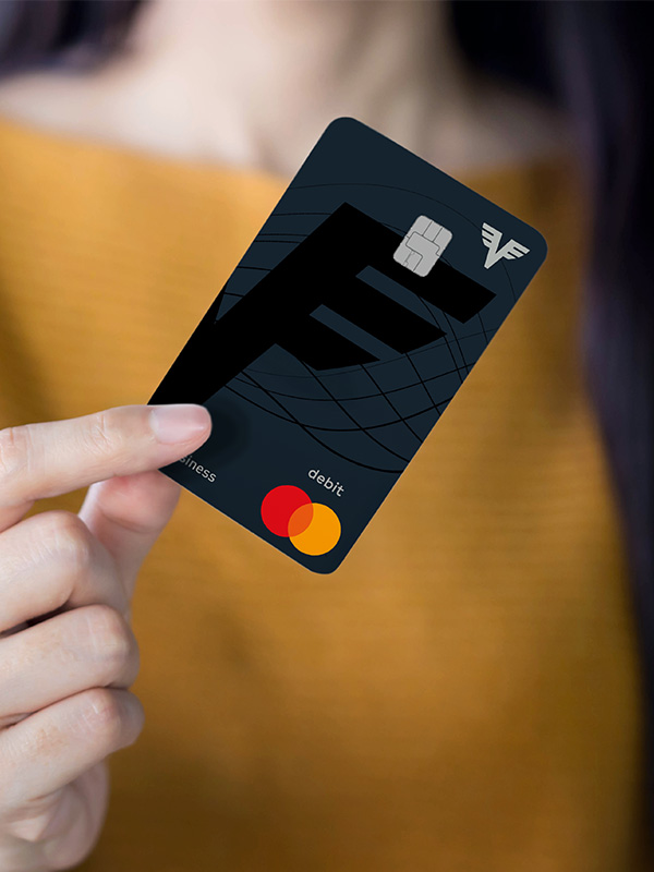 Eine Frau in einem gelben Pullover hält die Volksbank Debit Mastercard Business in der Hand. Man kann ihr Gesicht nicht sehen.