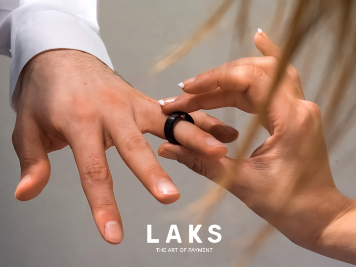 LAKS Pay Rind wird auf den Finger einer Hand geschoben. Davor verdecken getrocknete Gräser dezent die Sicht.