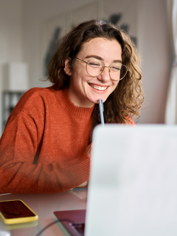 Eine Frau sitzt an ihrem Schreibtisch vor einem Notebook. Sie hat die Augen geschlossen und lächelt.
